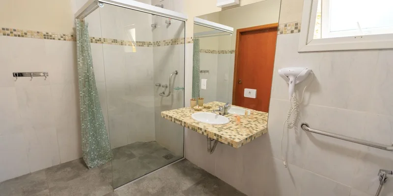 A spacious accessible home bathroom with a wall mounted grab bar, wide open floor space and a curbless shower in soft morning light.