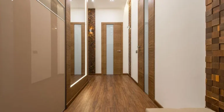 A wide open interior doorway with the door swung fully back against the wall and pale oak flooring running through into a bright hallway.
