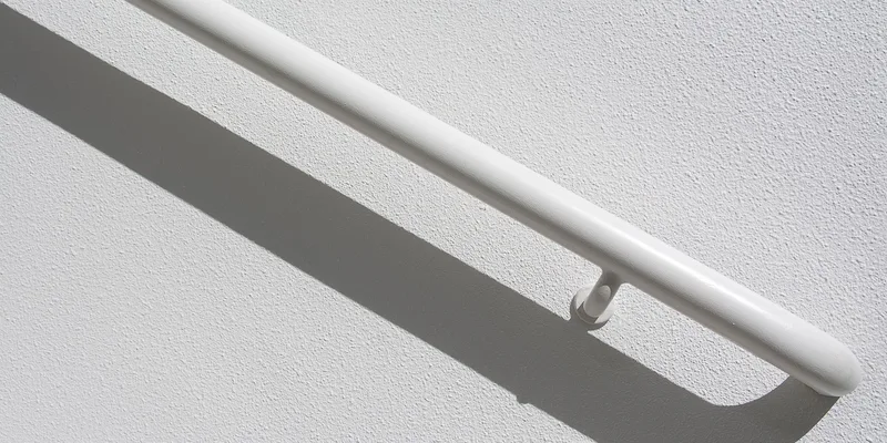 A stainless steel grab bar mounted horizontally on white subway tile above the rim of a bathtub.