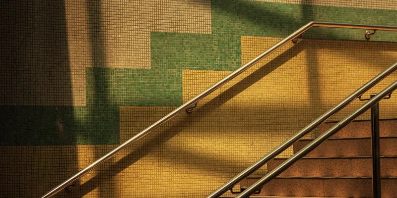 A smooth round wooden handrail on metal brackets running along a painted wall beside a carpeted indoor staircase.