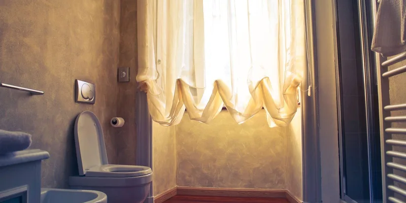 A tall white comfort height toilet in a bright bathroom with a grab bar on the side wall.
