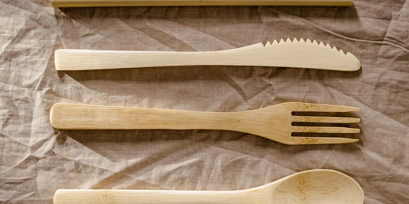 A set of eating utensils with thick built up foam handles arranged on a linen napkin on a dining table.