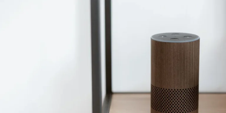 A small fabric covered smart speaker on a wooden dresser beside a table lamp in a warm living room.