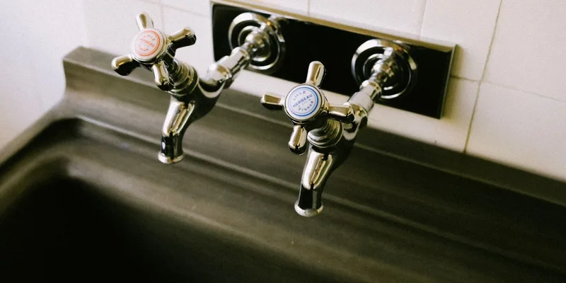 A chrome thermostatic shower valve trim and a handheld shower head on a tiled shower wall.