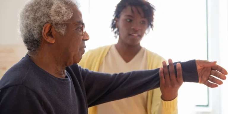 A caregiver supports an older man's arm during an exercise.