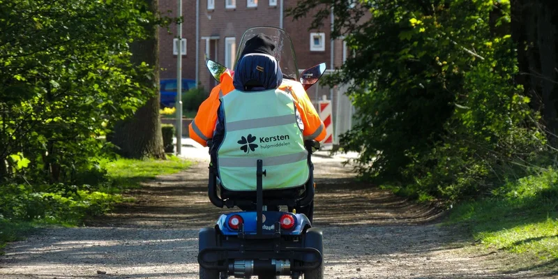 A rider on a sturdy four-wheel mobility scooter on a tree-lined path.