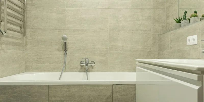 A powered bath lift seat lowered inside a white bathtub with its waterproof hand controller resting on the tub rim.