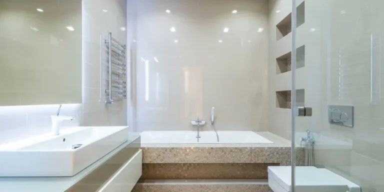 A shower chair, handheld shower head, long handled sponge and wall grab bar together in a bright tiled bathroom.