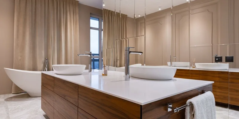 A compact bathroom with grab bars beside the toilet and tub, a plug in night light and a non slip mat, lit through frosted glass.