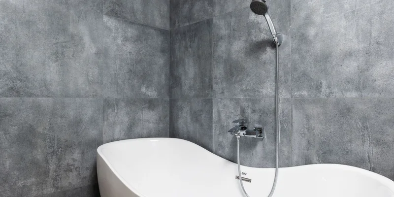 A clamp on tub rail gripping the rim of a white bathtub in a tiled bathroom.