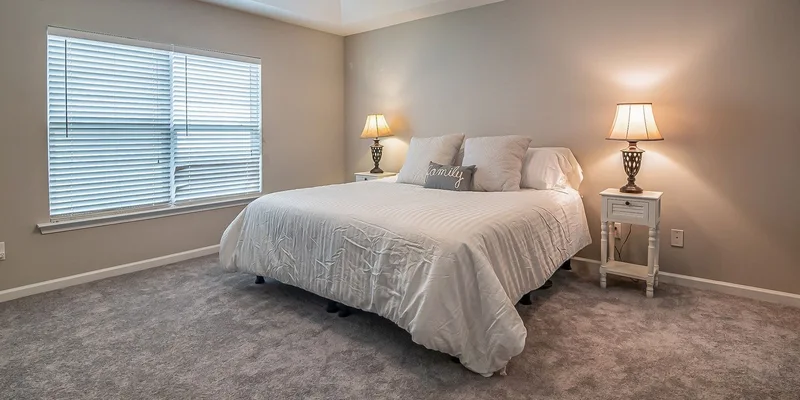 A queen bed with a swing down bed rail beside a nightstand in a bright bedroom.