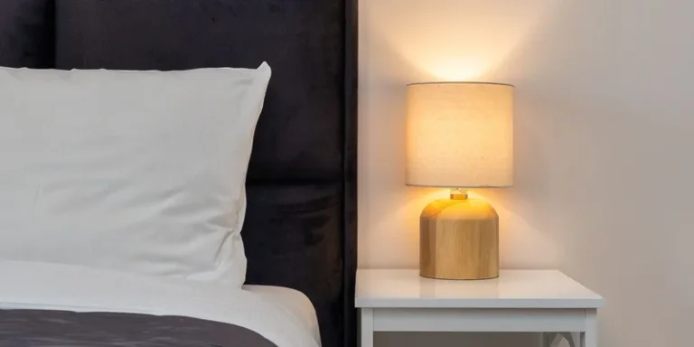A touch activated bedside lamp glowing softly on a nightstand next to a small puck light.