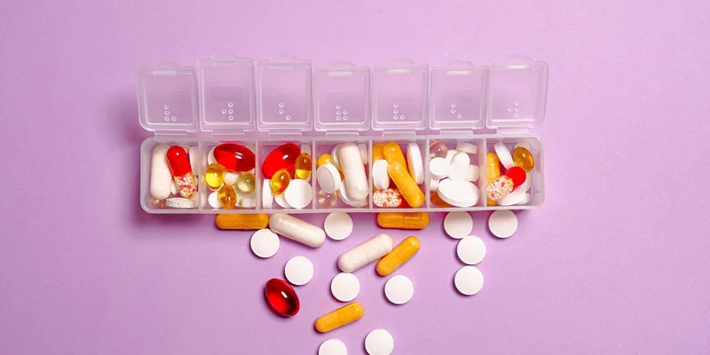 A round automatic pill dispenser with a locking lid on a kitchen counter beside a glass of water.