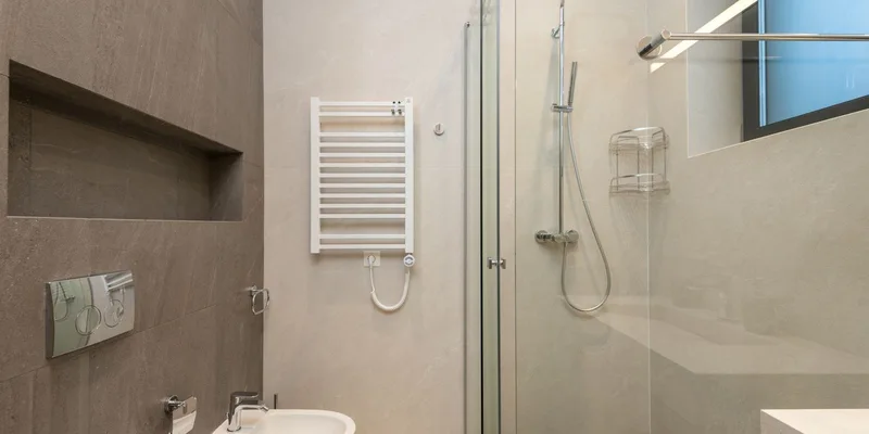 A bidet attachment on a toilet with a long handled wiping aid resting on the counter beside it.