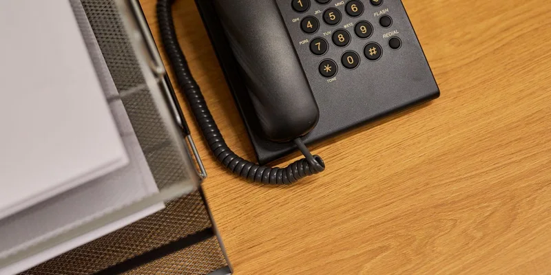 A corded phone with oversized number keys on a side table beside an armchair.