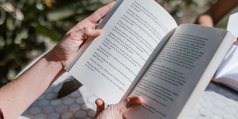An adjustable book holder cradling an open book with blank pages on a table beside a reading chair.