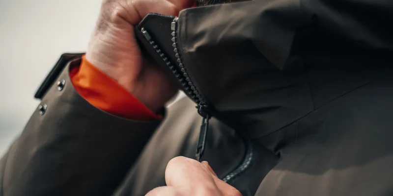 A button hook and a looped zipper pull lying on a folded shirt on a bedroom dresser.