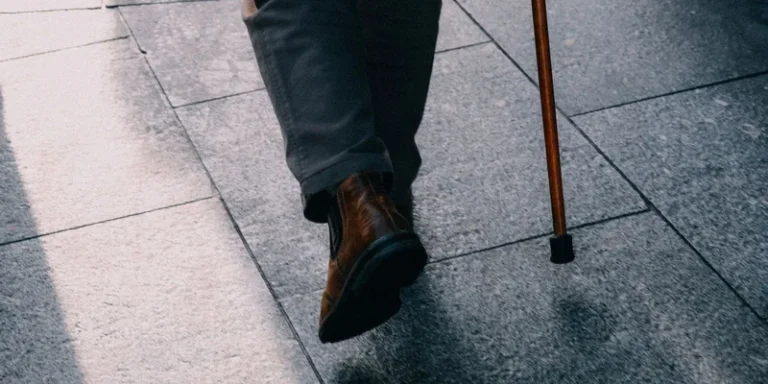 Replacement rubber cane tips, a wrist strap and a clip on holder arranged on a wooden table beside a walking cane.