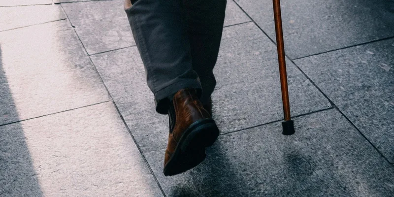 Replacement rubber cane tips, a wrist strap and a clip on holder arranged on a wooden table beside a walking cane.