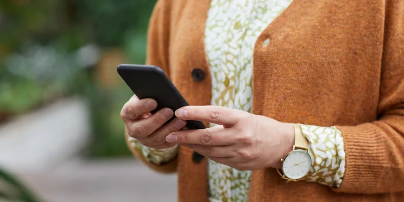 A smartphone and a simple flip phone lying side by side on a wooden dresser.