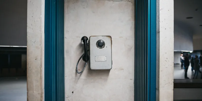 A cordless phone handset in its charging base on a kitchen counter with a second handset on a hallway table.