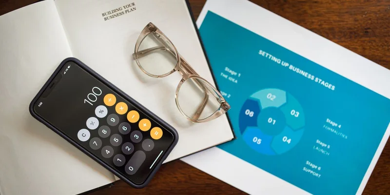 A calculator, glasses and notes laid out on a desk.