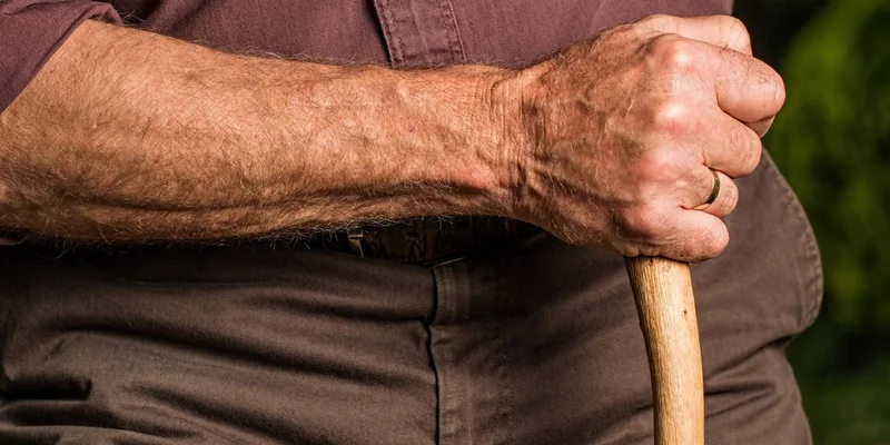 An older person's hand resting on the handle of a wooden cane.