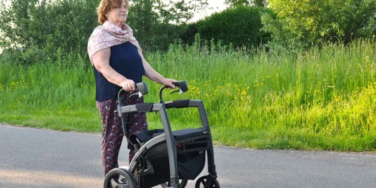 A woman walks outdoors with a rollator on a country road.