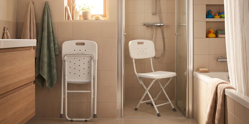 A folding shower chair set up in a shared family bathroom with a second chair folded flat against the wall.