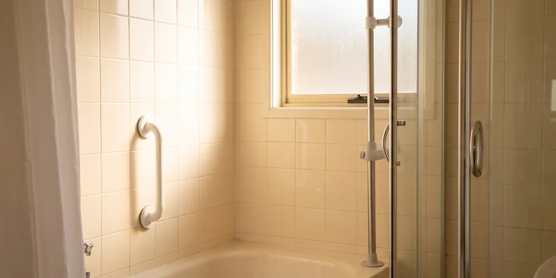 A suction grab bar and a tension mounted pole in a rental bathroom with no drilled holes.