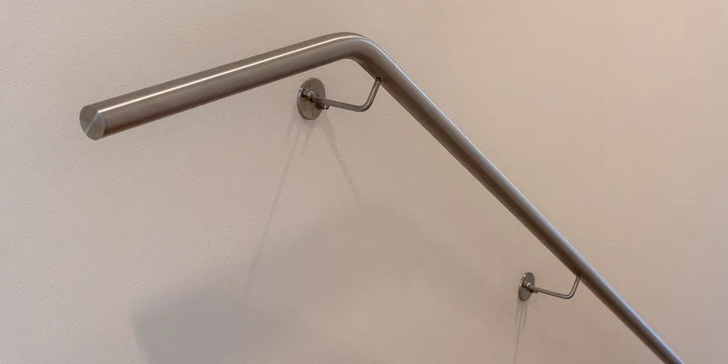 Two grab bars mounted inside a tiled shower, one horizontal on the back wall and one vertical at the entry.