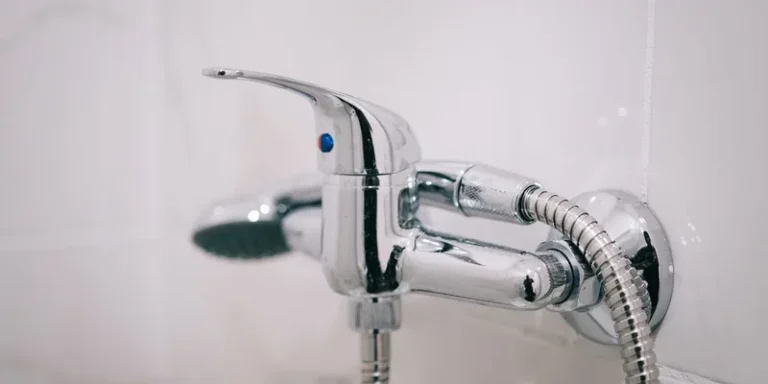 A handheld shower head on a sliding bar with a long hose in a tiled shower.