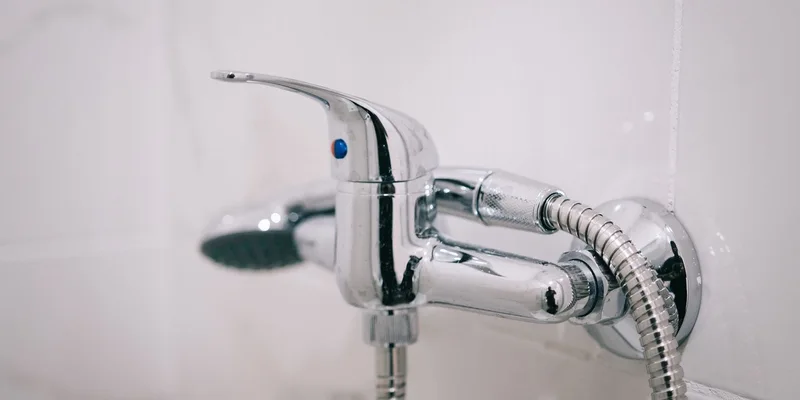 A handheld shower head on a sliding bar with a long hose in a tiled shower.