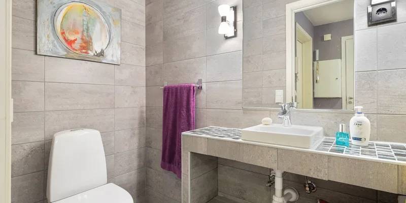 A raised toilet seat with its clamp brackets loosened resting on a toilet bowl.