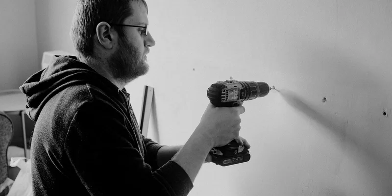 A cordless drill, a spirit level and a grab bar laid out on a towel beside a tiled bathroom wall.
