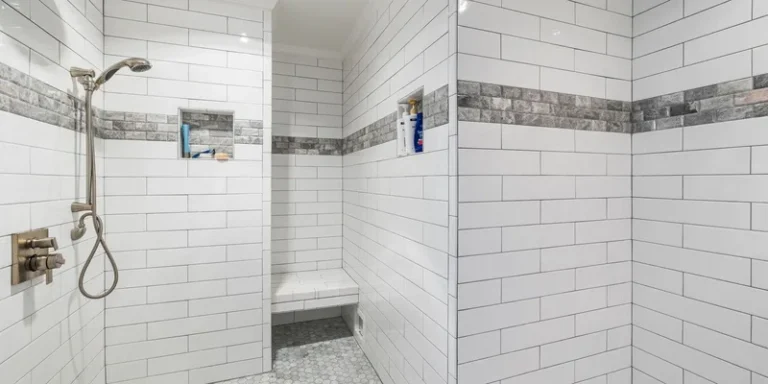 A home shower fitted with a grab bar, a seat, a non slip mat and a handheld shower head.