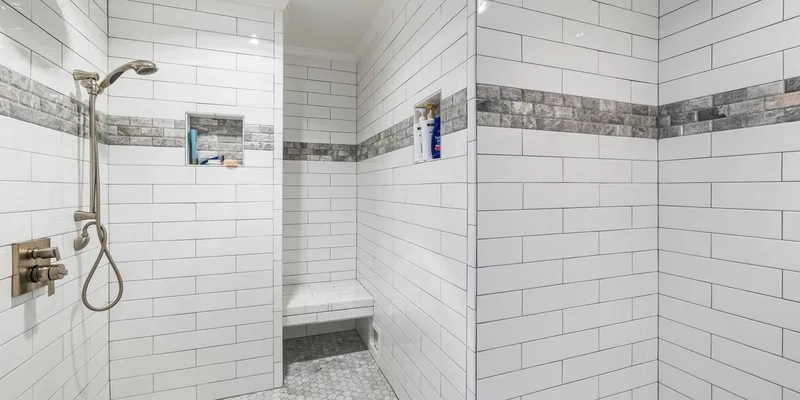 A home shower fitted with a grab bar, a seat, a non slip mat and a handheld shower head.