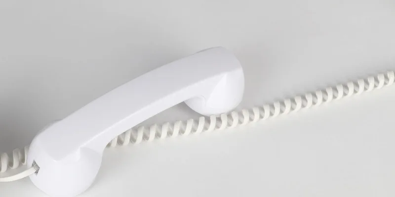 A corded landline phone on a hallway table with its cord neatly coiled.