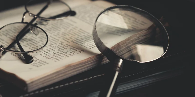 A lighted handheld magnifier and a stand magnifier on a desk beside a lamp.
