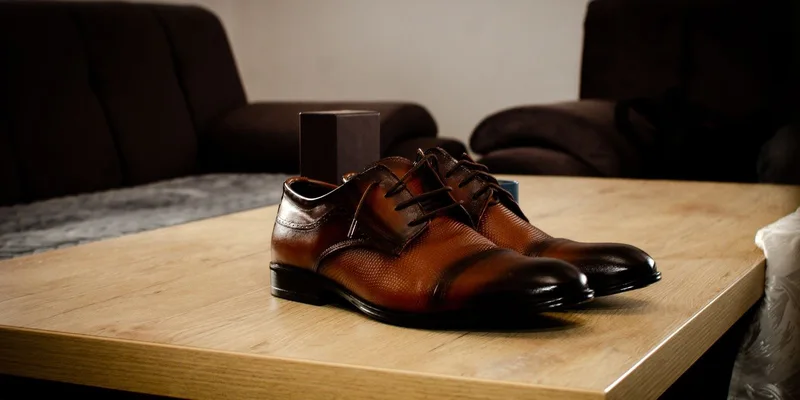 A long metal shoe horn leaning in a mudroom corner beside a pair of shoes.