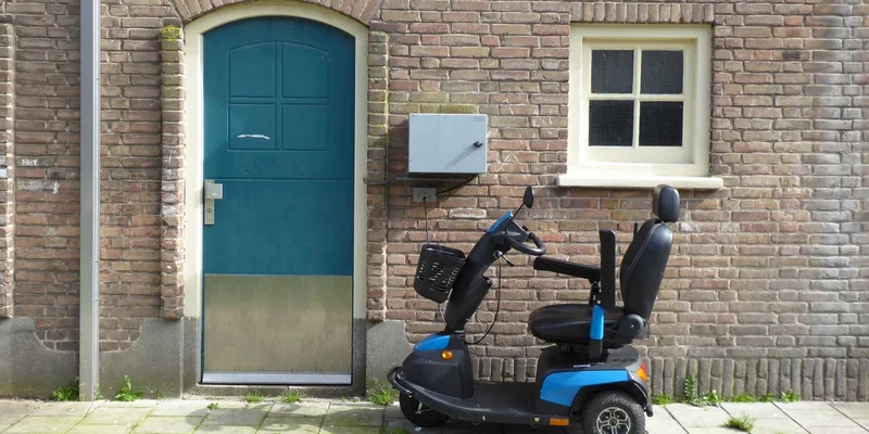 A mobility scooter with a seat and armrests parked outside a house.