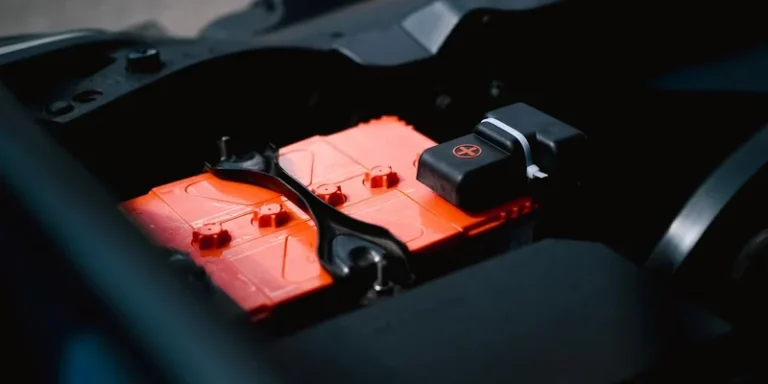 A vehicle battery with connected terminals under an open hood.