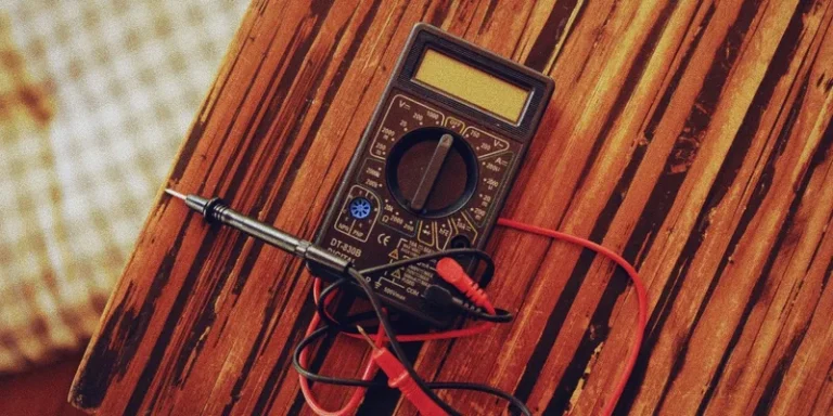 A digital multimeter with test leads on a wooden table.