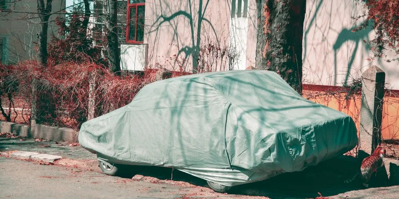 A vehicle parked outdoors under a fitted protective cover.