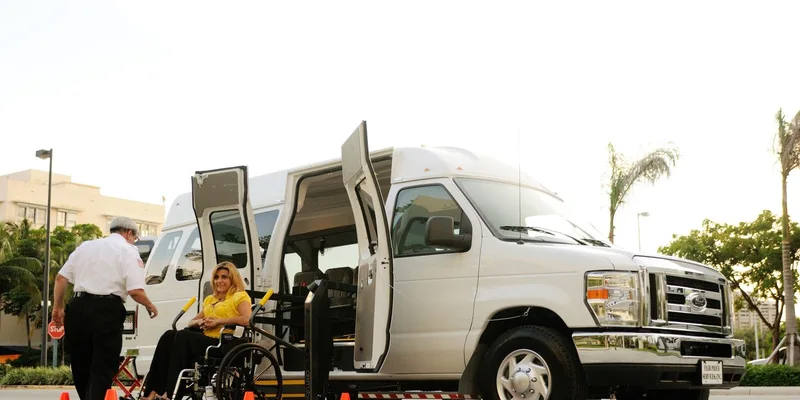 A seated passenger boards a van using a powered lift.