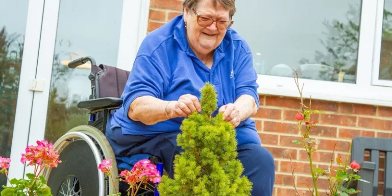 A seated older woman tends plants in her garden.