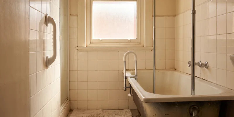 A suction grab bar, a clamp on tub rail and a tension pole grouped in a rental bathroom.