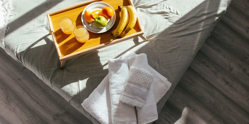 A height adjustable overbed table with a tilting top rolled across the side of a bed.
