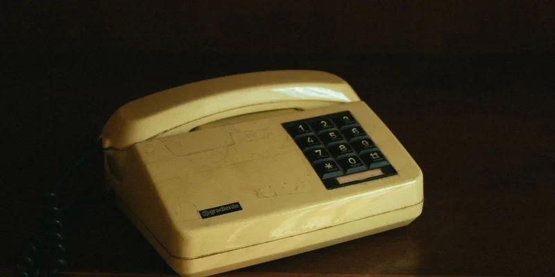 A corded phone, a cordless handset and a smartphone lined up on a console table.