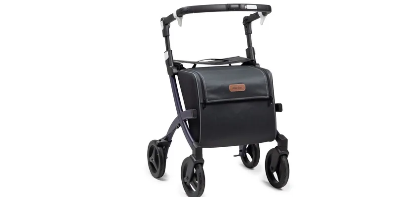 A rollator fitted with a basket, a cane holder and a cup holder standing in a hallway.